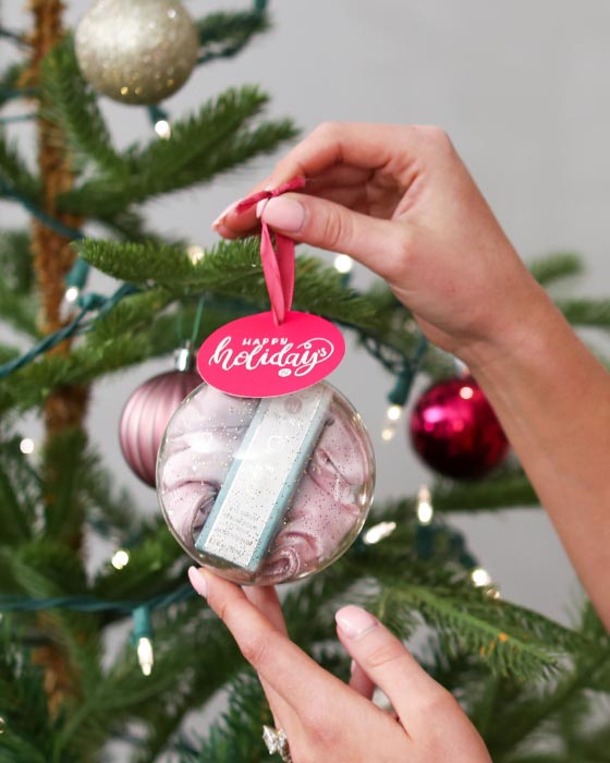 Woman holding Neora’s hottest holiday must-have, the All Eyes on You Set, which includes Age IQ® Eye Serum, Eye-V™ Moisture Boost Hydrogel Patches and FREE Eye Mask next to a Christmas tree.